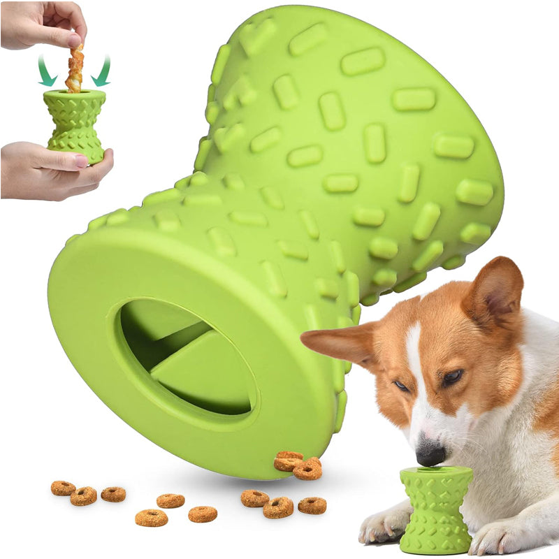 Hands stuffing a chew stick into the green rubber chew toy while a corgi eats kibble beside it
